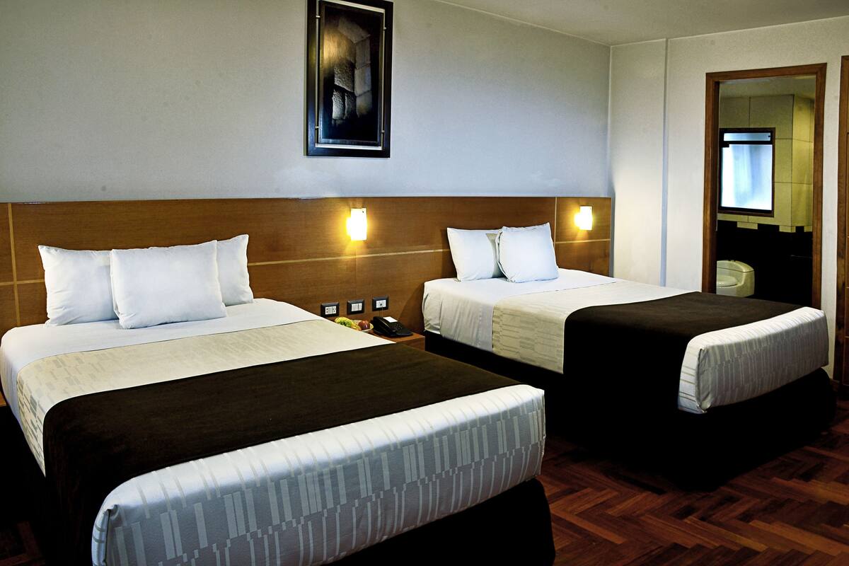 Ein Hotelzimmer mit zwei Betten, jeweils mit weißer Bettwäsche und braunen Kopfteilen. Über den Betten befinden sich Wandleuchten und an der Wand ein gerahmtes Bild.