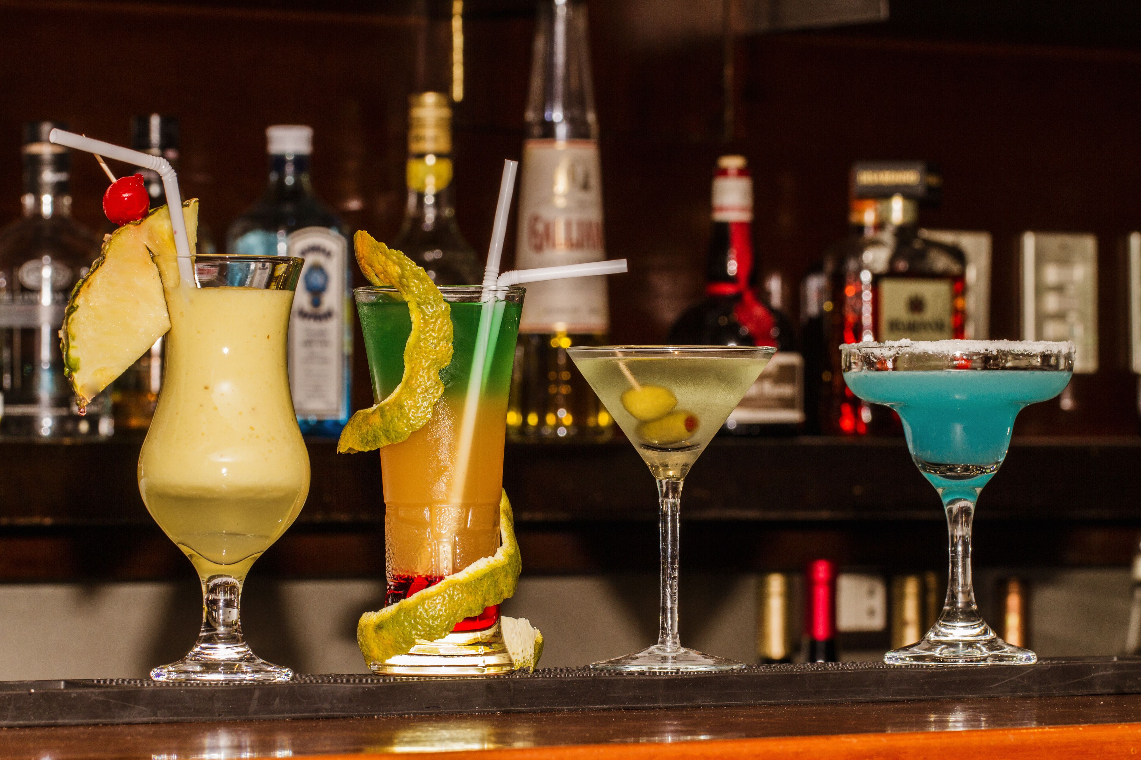 Een bar met vier verschillende cocktails, elk met unieke garneringen en rietjes.