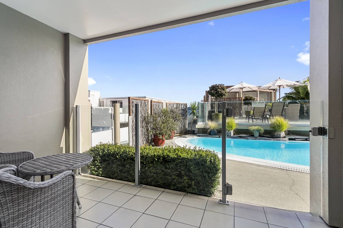 A balcony with wicker furniture, a swimming pool, and a 'POOL HOURS' sign.