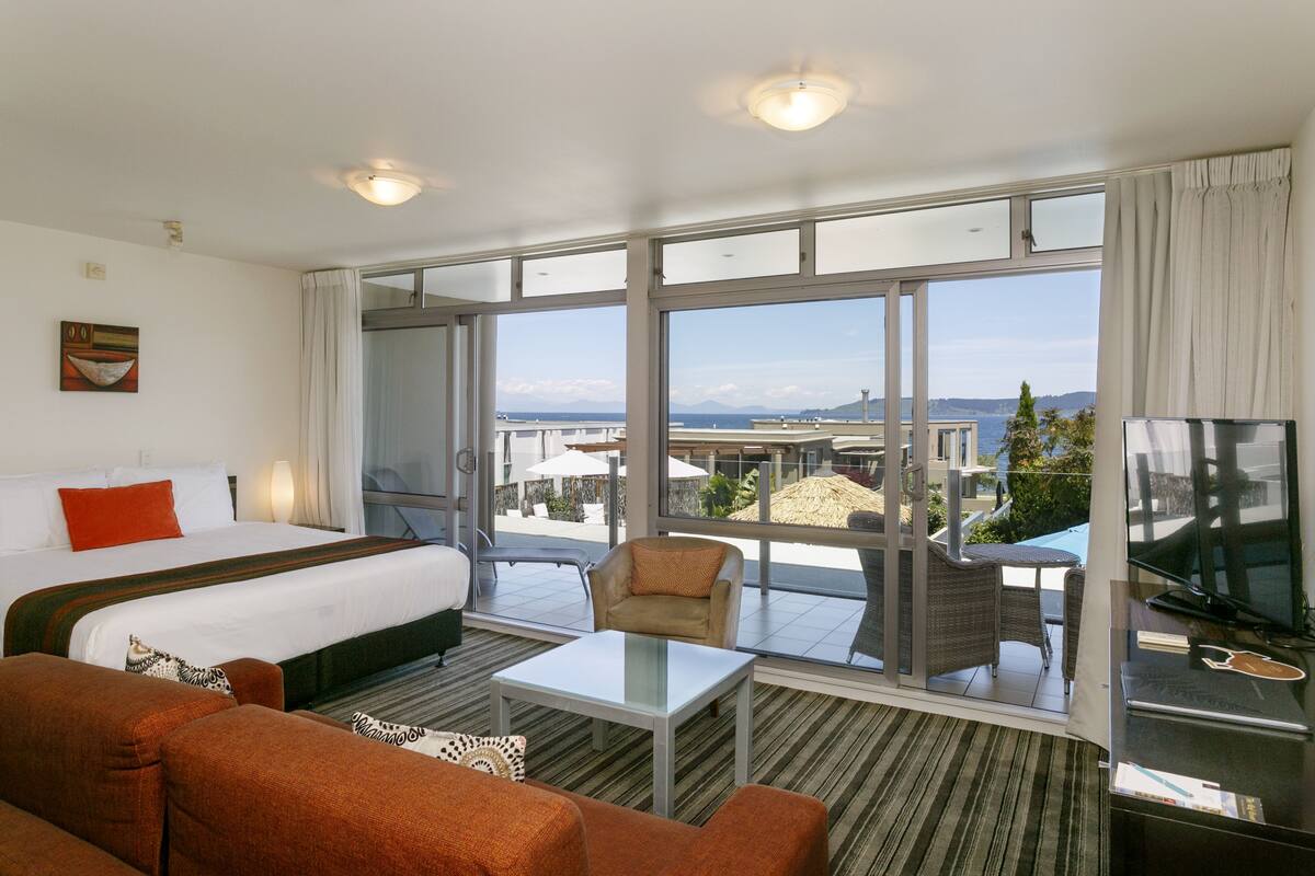 A hotel room with a large bed, a sofa, a TV, and a balcony with a view of the city.