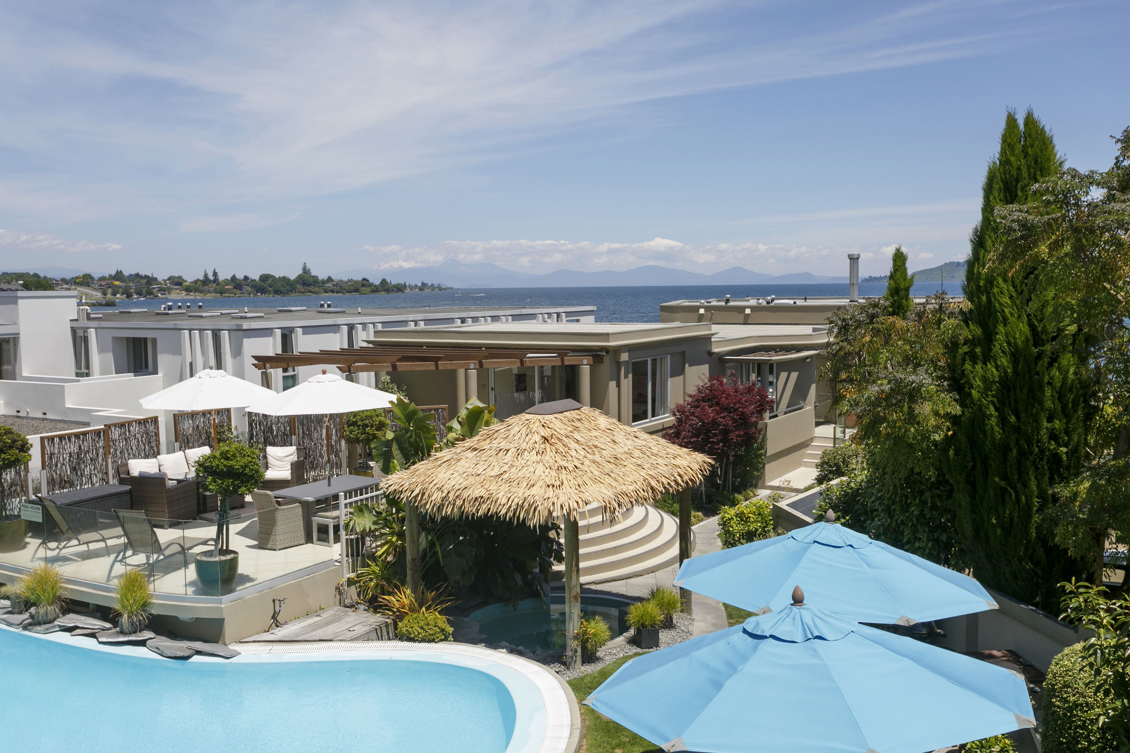 Área de piscina en la azotea con sillones de descanso, sombrillas y vistas al mar y a las montañas.