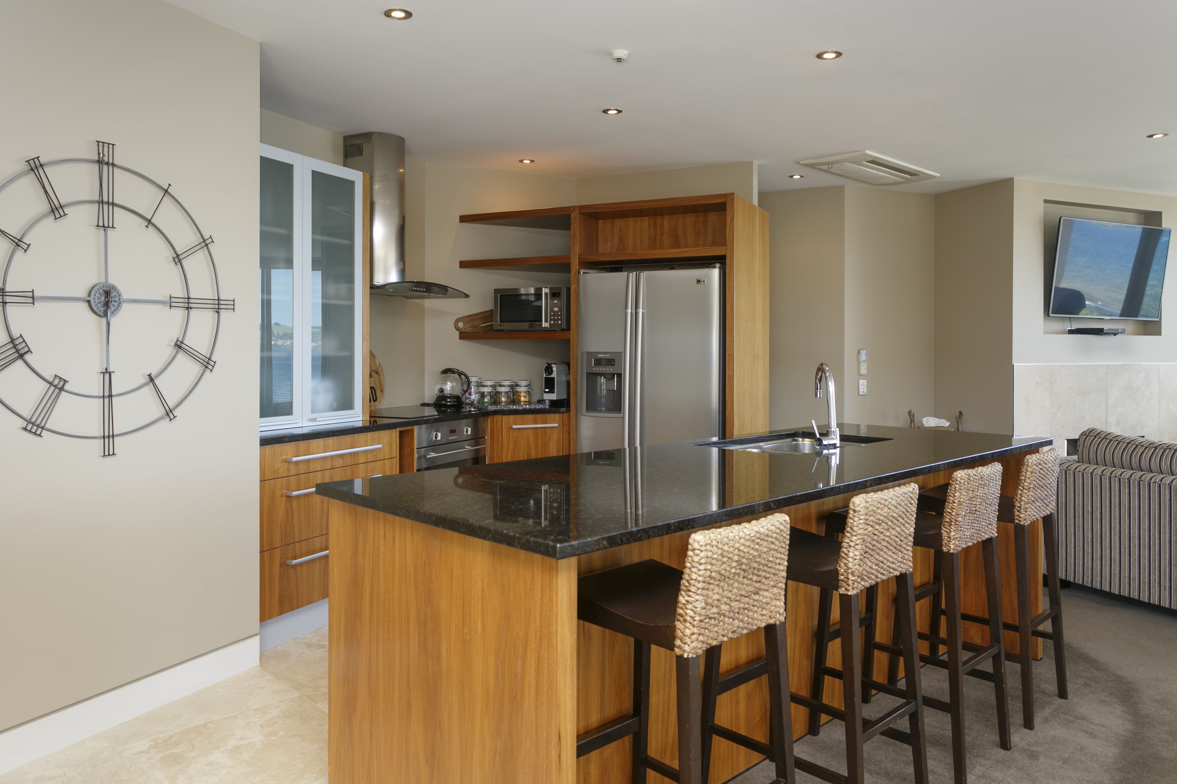 Une cuisine moderne dotée d’un îlot central, de meubles en bois, d’appareils électroménagers en acier inoxydable et d’une grande horloge murale.