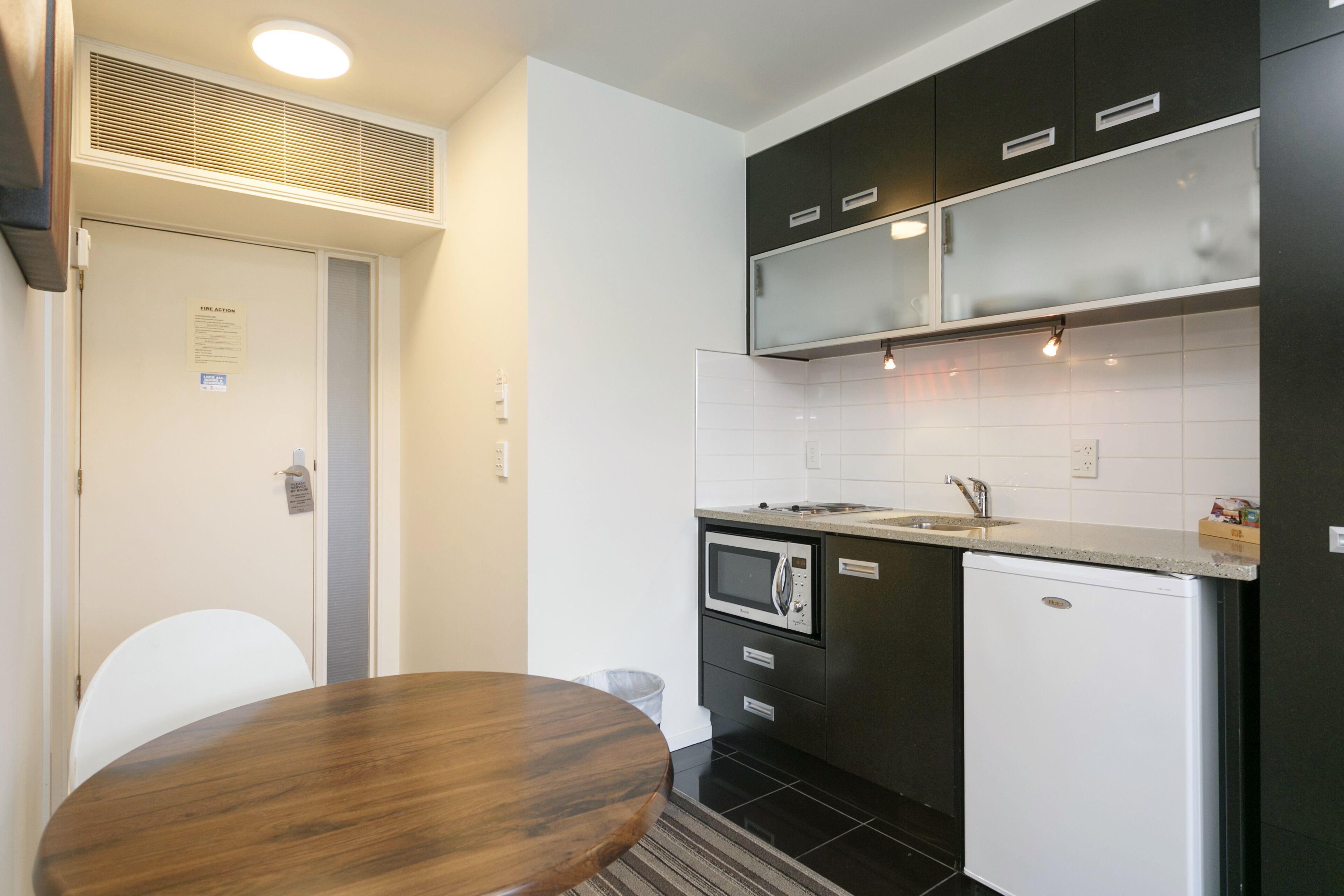 Una cocina compacta con microondas, lavamanos y armarios negros.