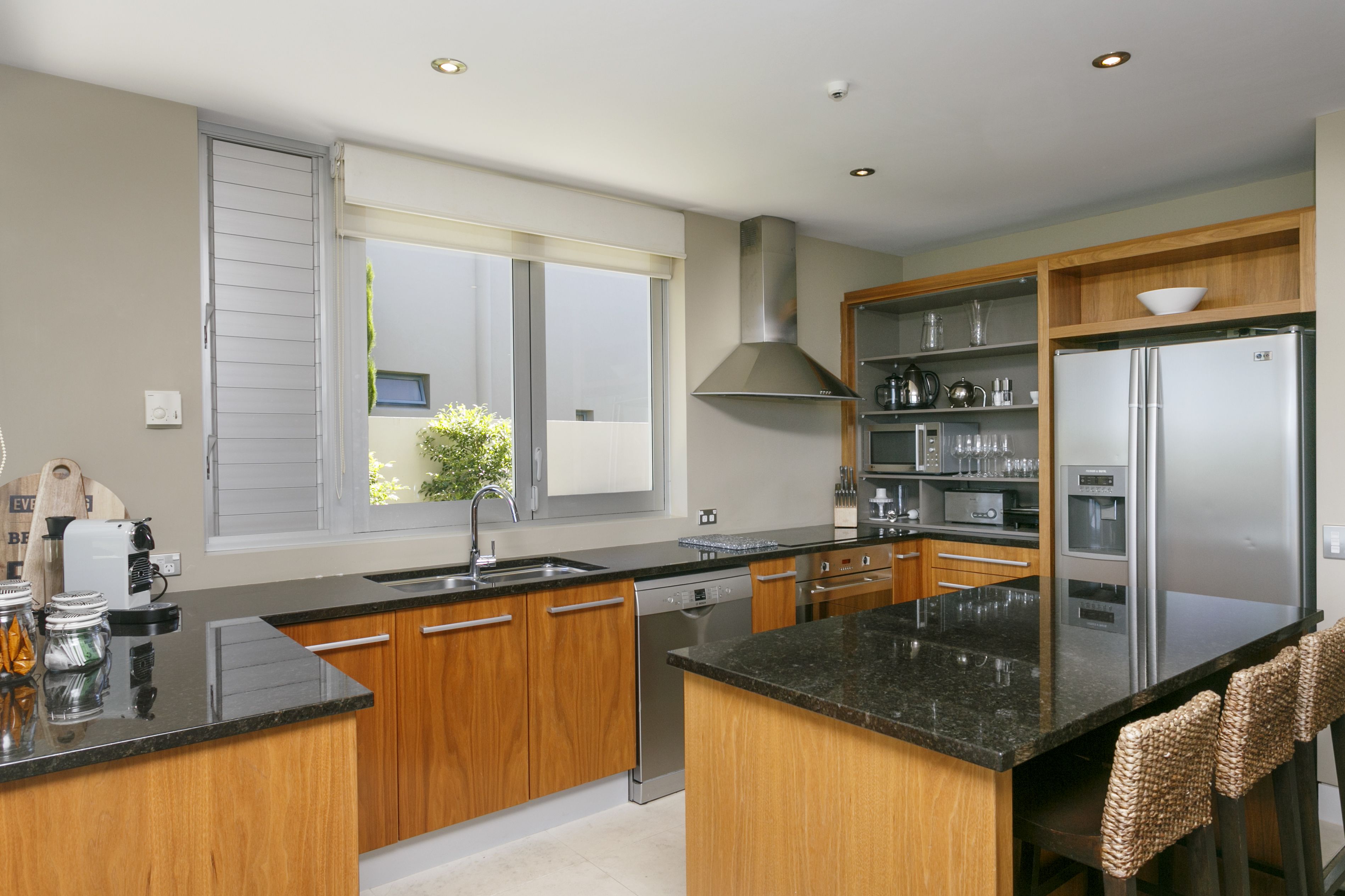 A modern kitchen with wooden cabinets, a stainless steel refrigerator, and a large window.