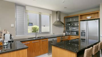 A modern kitchen with wooden cabinets, a stainless steel refrigerator, and a large window.