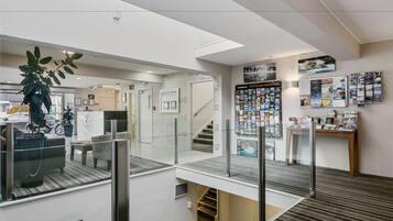 A modern hotel lobby with a glass railing, a staircase, and a wall displaying various brochures and a 'Visitor Information' sign.