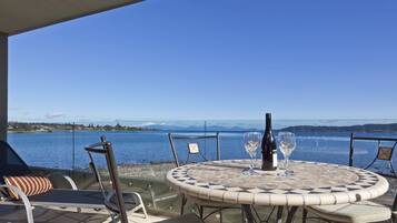 A round table with a mosaic pattern, two wine glasses, and a bottle of wine on a terrace overlooking a lake with mountains in the distance.