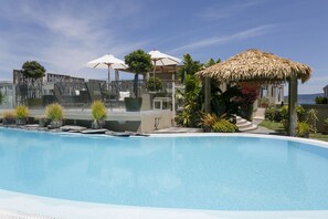 A swimming pool with a thatched-roof gazebo, lounge chairs, and umbrellas. - The Reef Resort (Taupo)