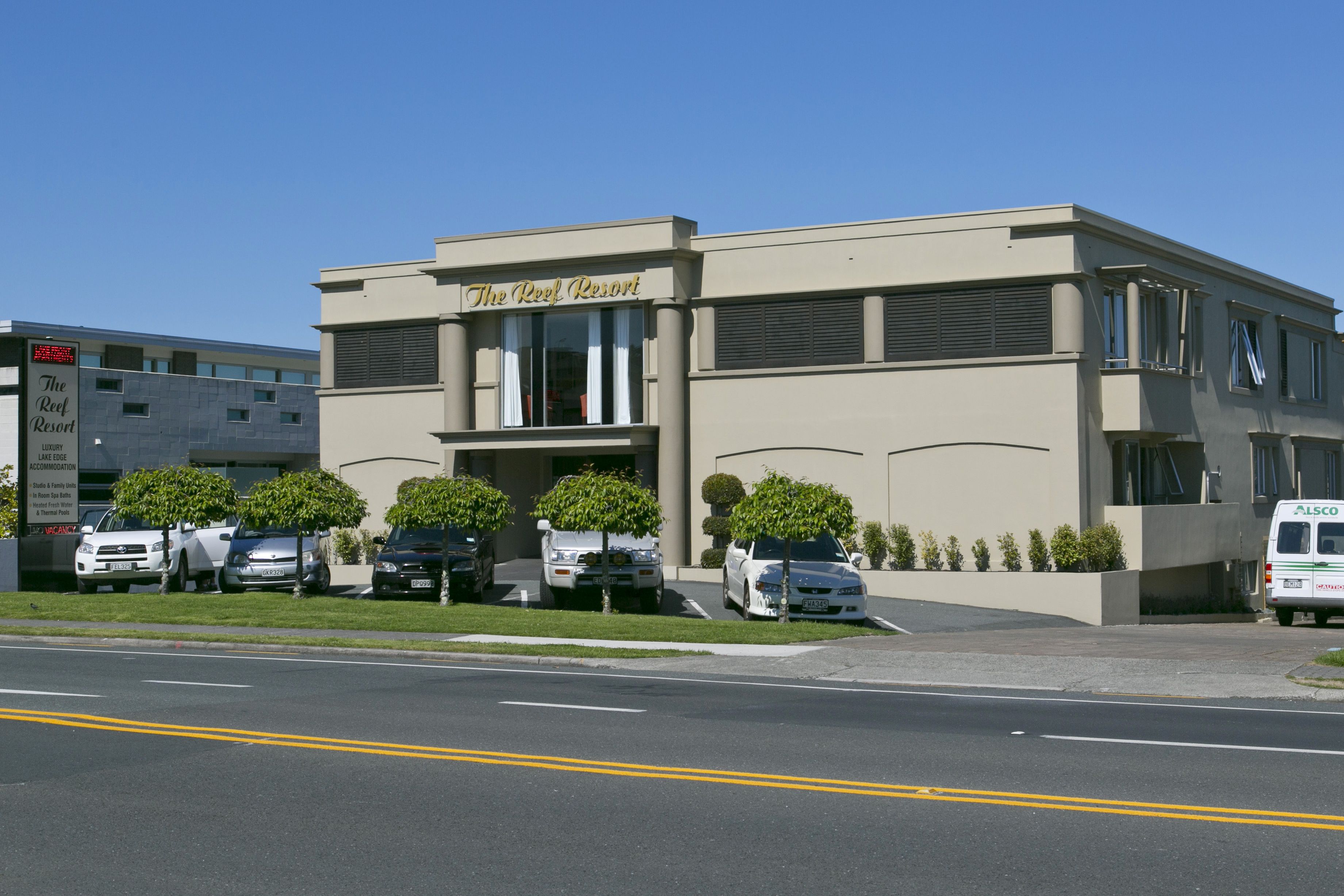 The Reef Resort with a modern facade, multiple parking spaces, and a clear blue sky.