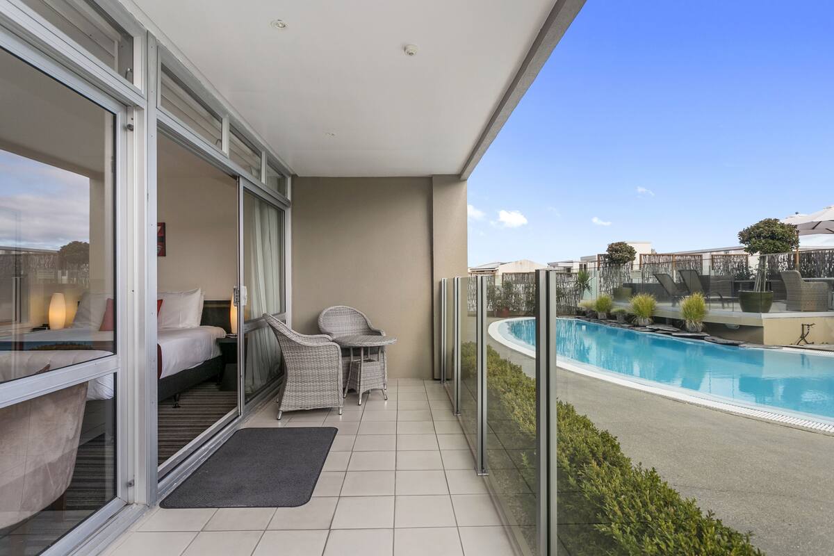 A balcony with a glass door leading to a bedroom, a pool, and a view of the surrounding area.
