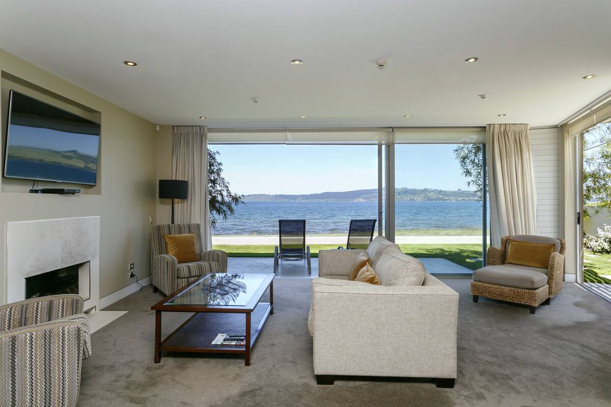 A living room with a large window overlooking a body of water, furnished with a sofa, armchairs, and a coffee table.