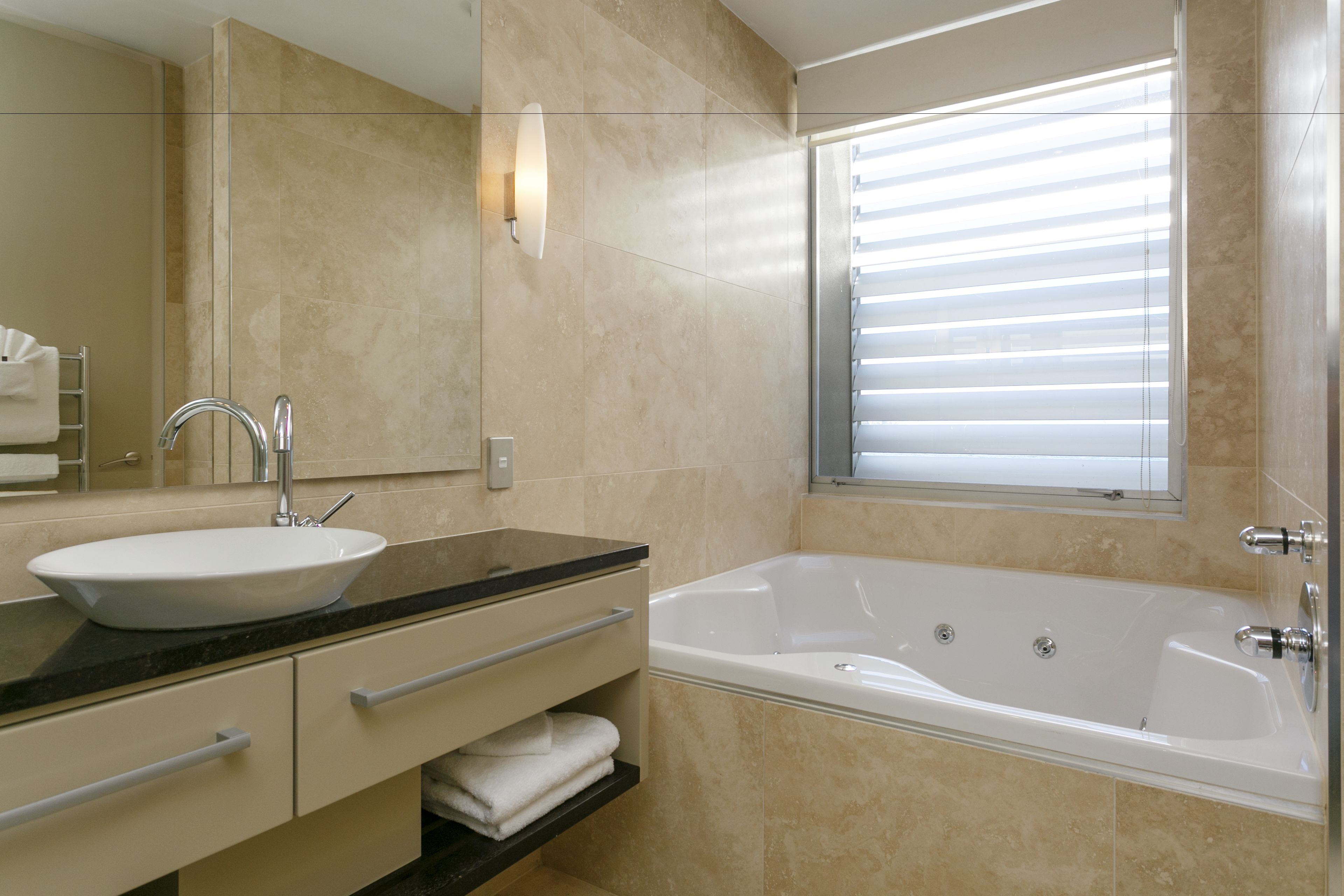 Une salle de bain moderne avec un grand lavabo, une baignoire et une fenêtre équipée de stores.
