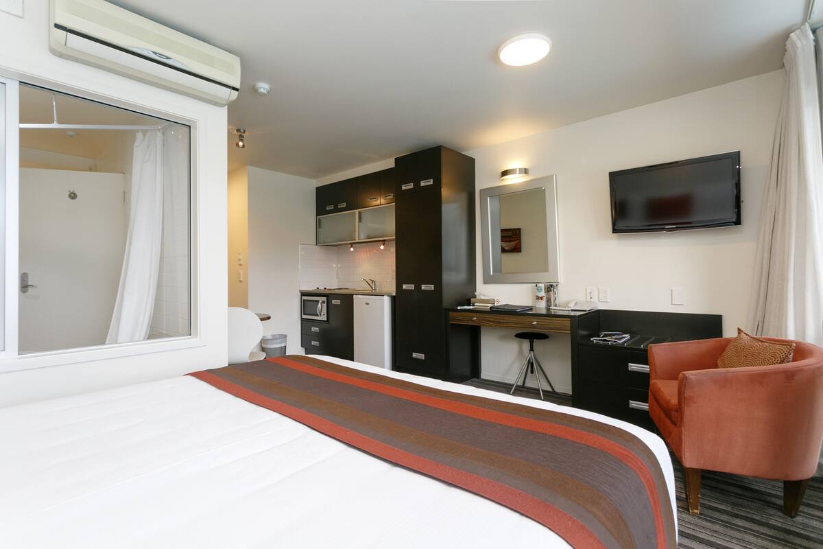 A compact hotel room with a bed, kitchenette, and a TV.