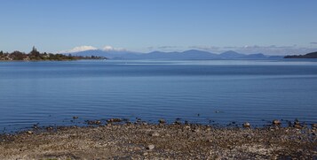 Un lago tranquilo con una orilla rocosa y montañas a lo lejos.