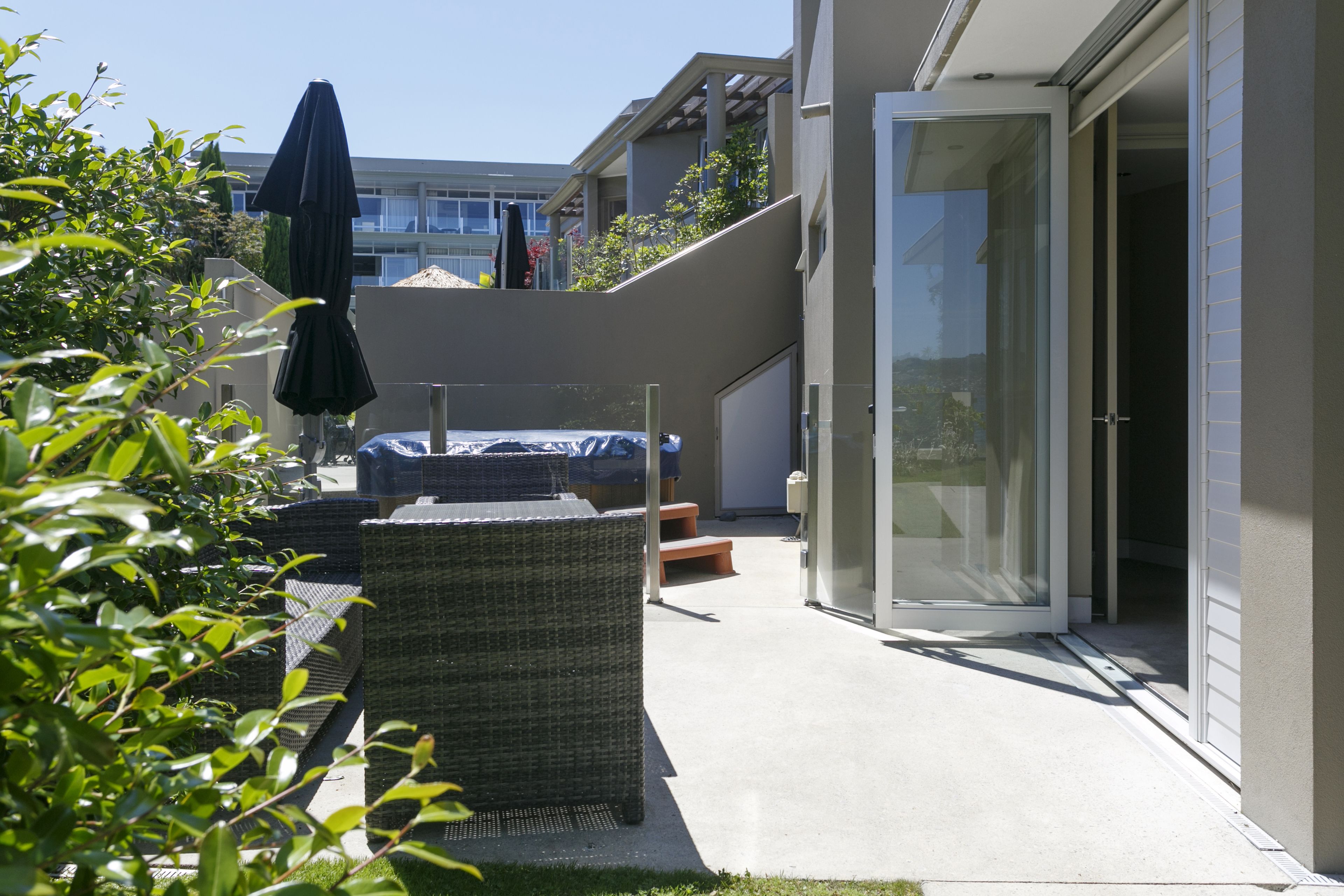 Een terras met rieten meubilair, een overdekte parasol en een glazen deur naar een overdekt buitengebied.