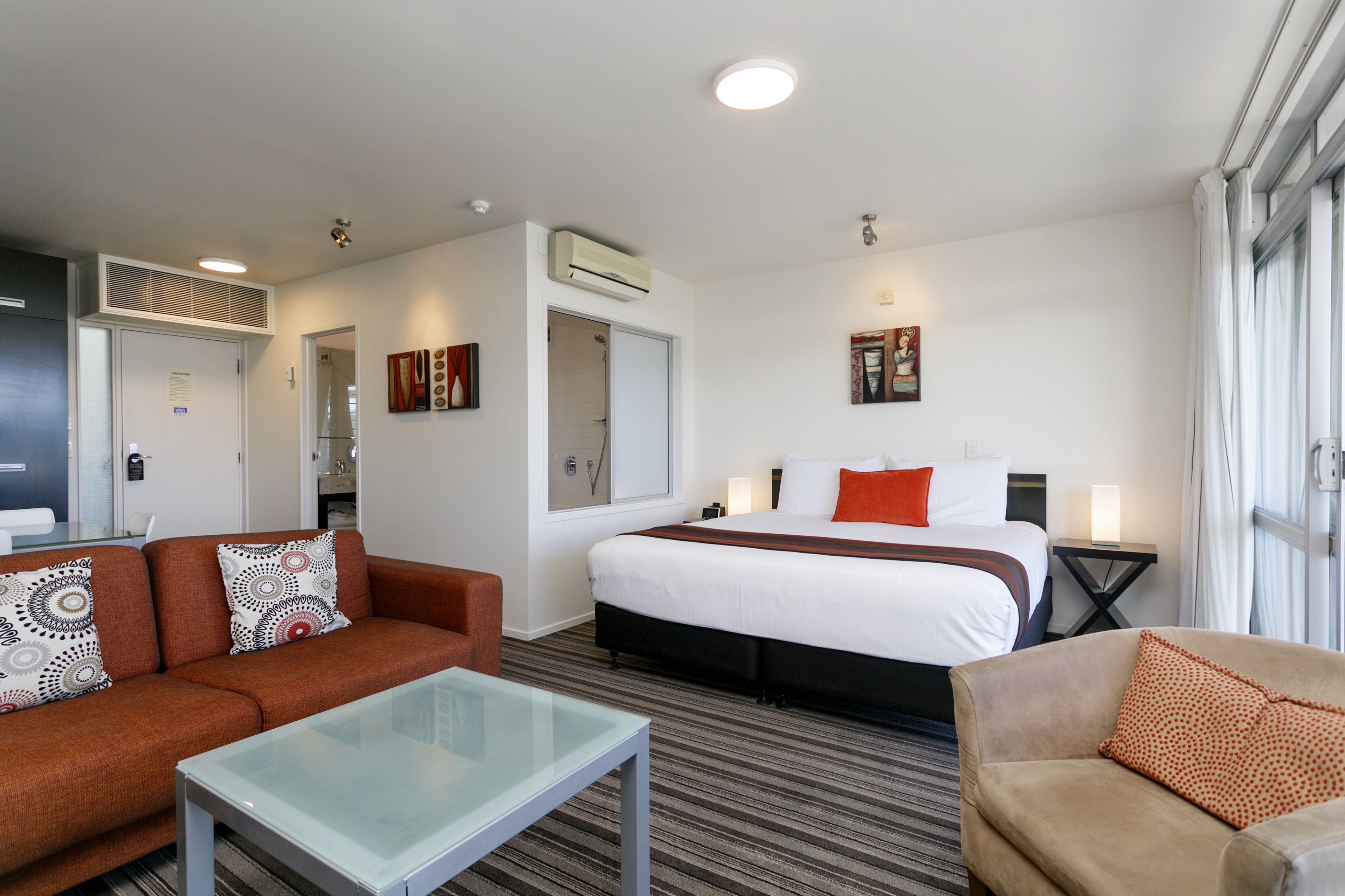 Une chambre d’hôtel comprenant un lit, deux canapés, une table basse en verre et une petite table avec une lampe.