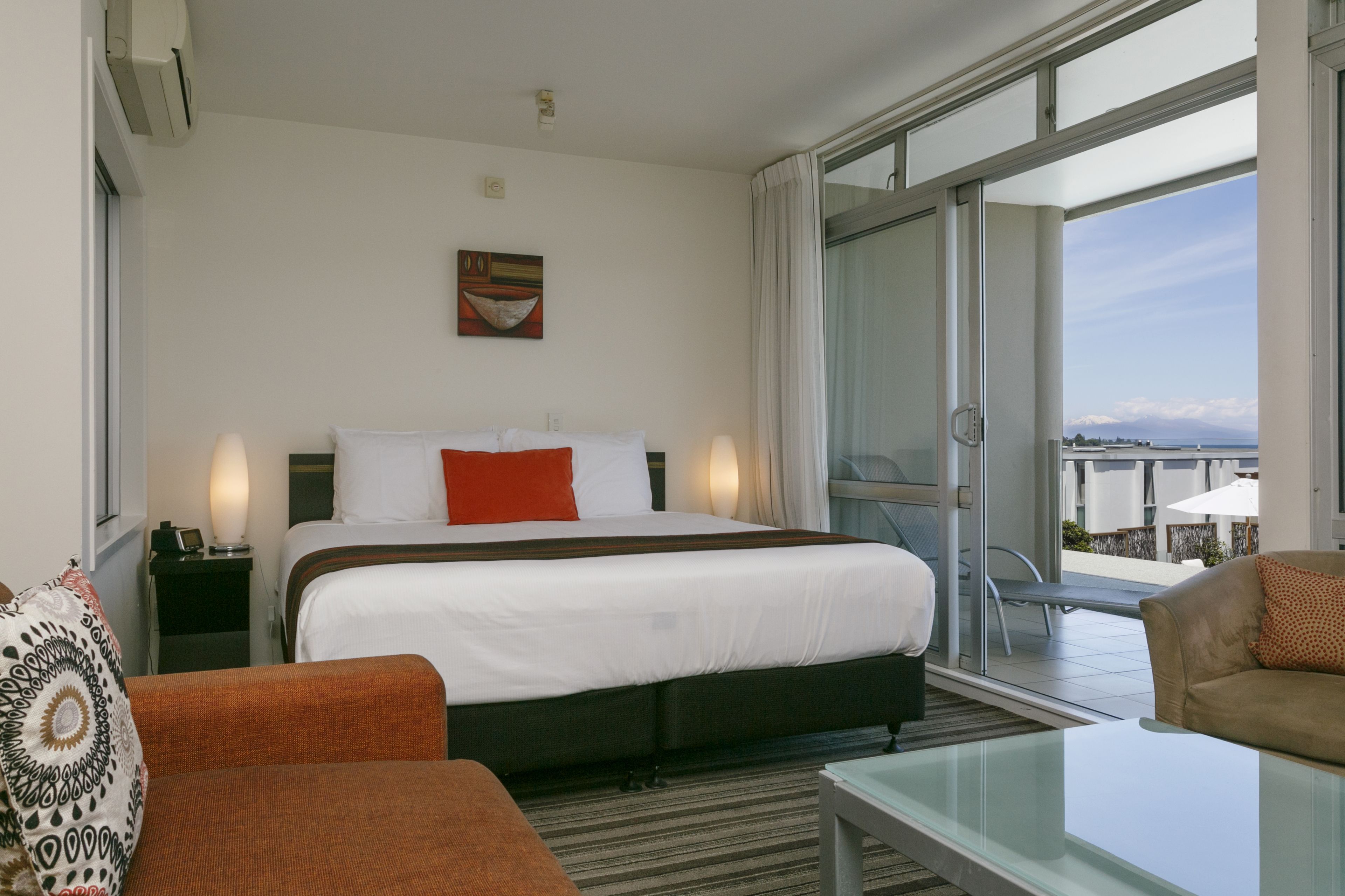 A hotel room with a large bed, a sofa, a glass table, and a balcony with a view.