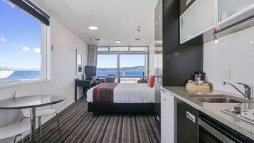 A hotel room with a bed, a desk, a chair, a small table, a sink, and a view of the sea.