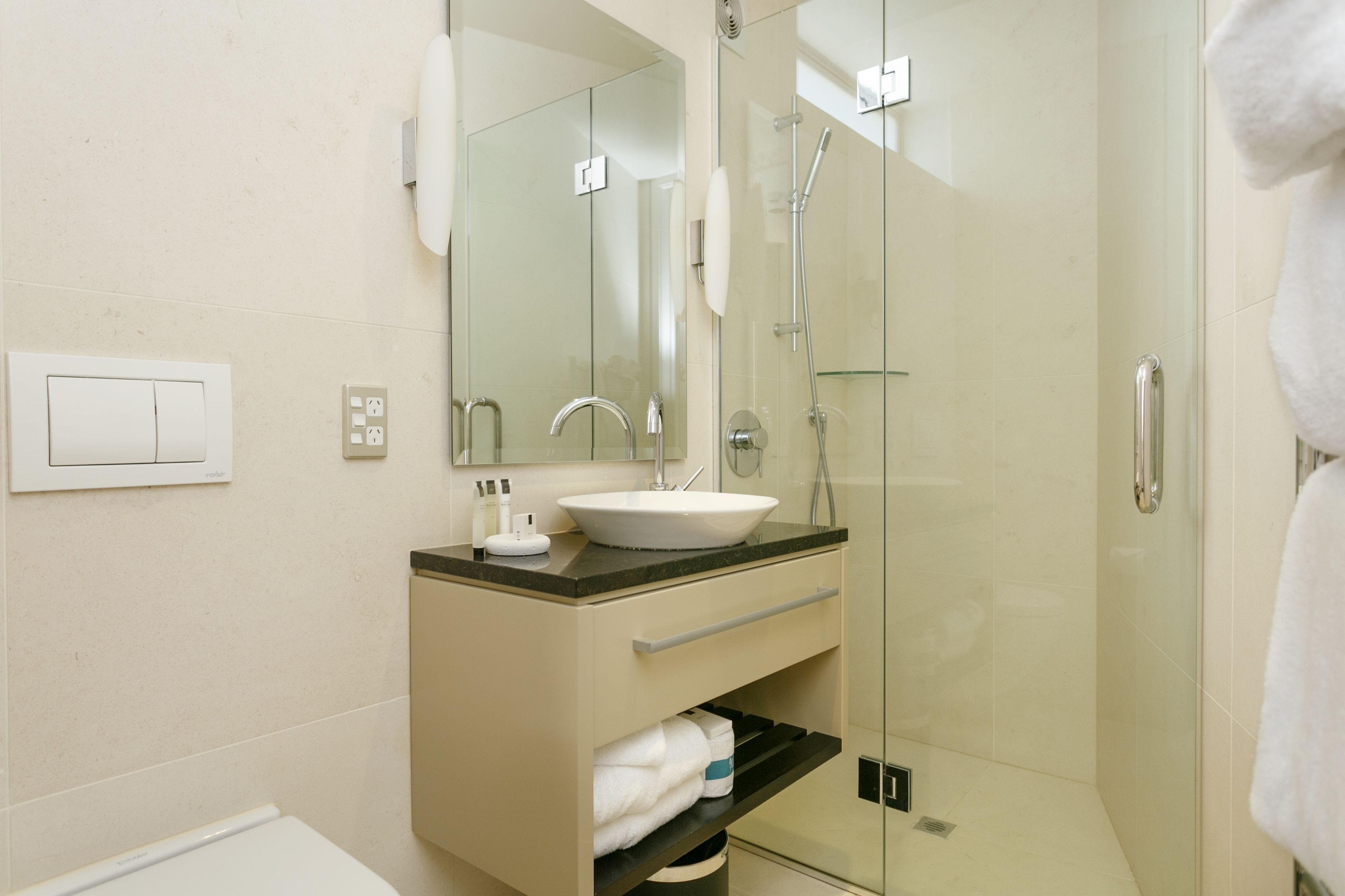 Een moderne badkamer met een douchecabine van glas, een witte wastafel en een badkamermeubel met een spiegel.