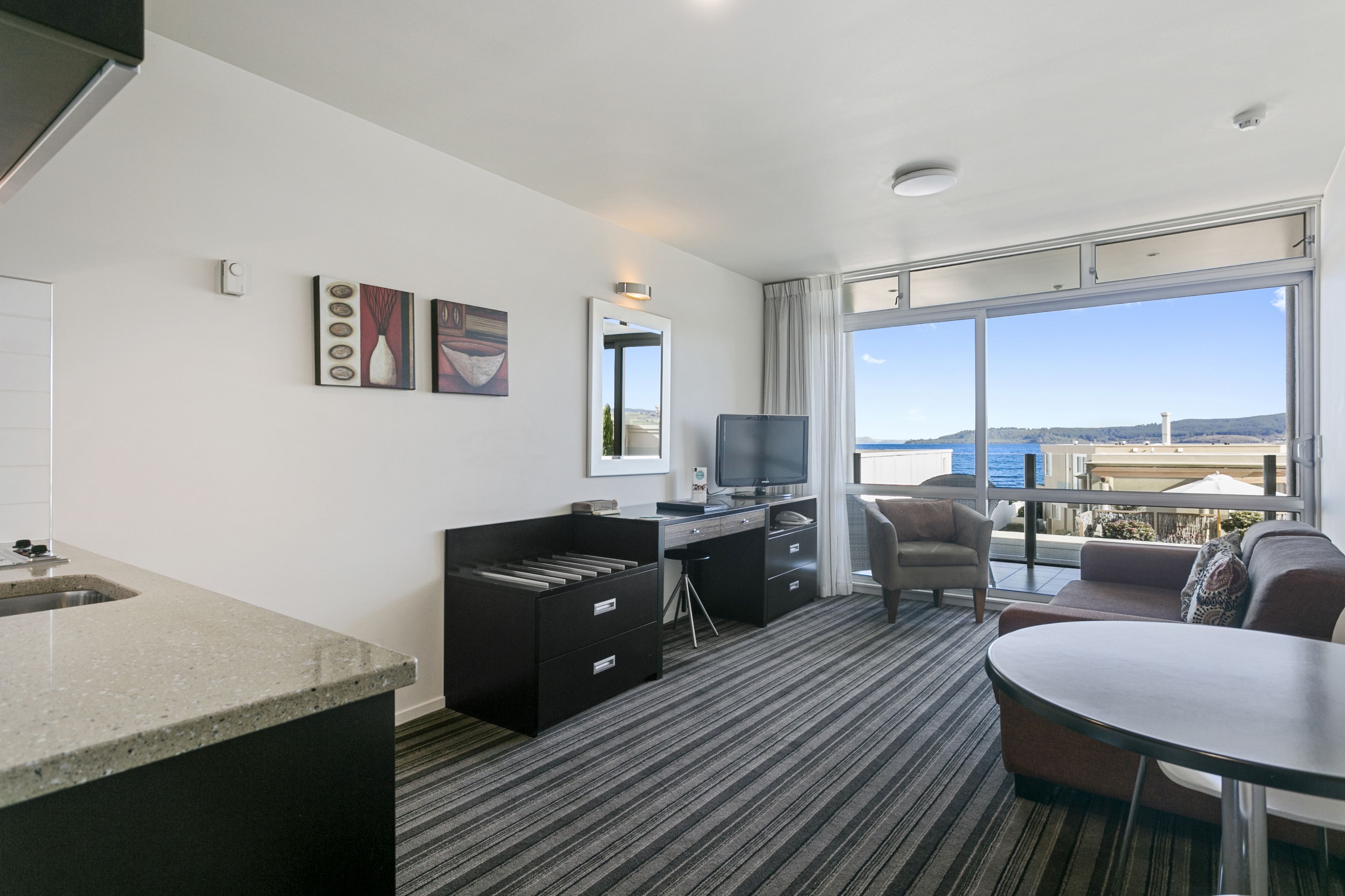 A hotel room with a desk, chair, and a large window offering a view of the sea.
