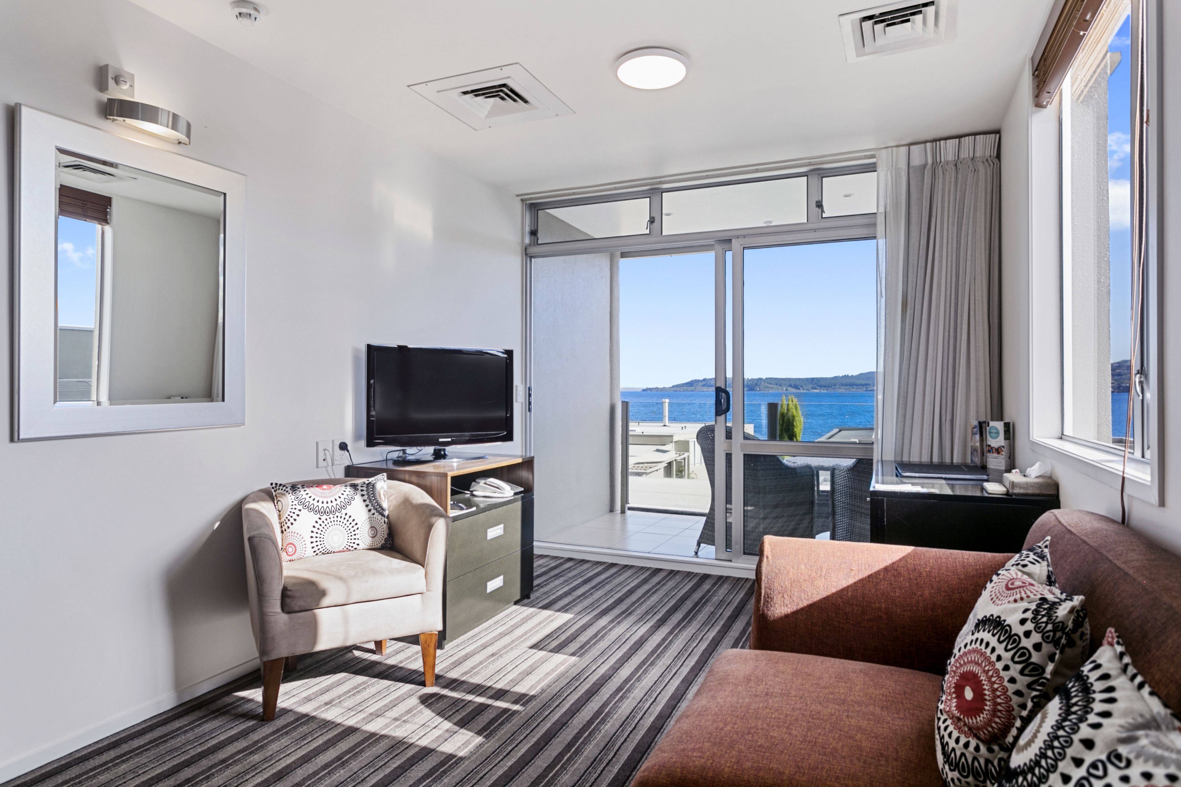 Een moderne hotelkamer met een grote schuifglazen deur die leidt naar een balkon met uitzicht op zee.