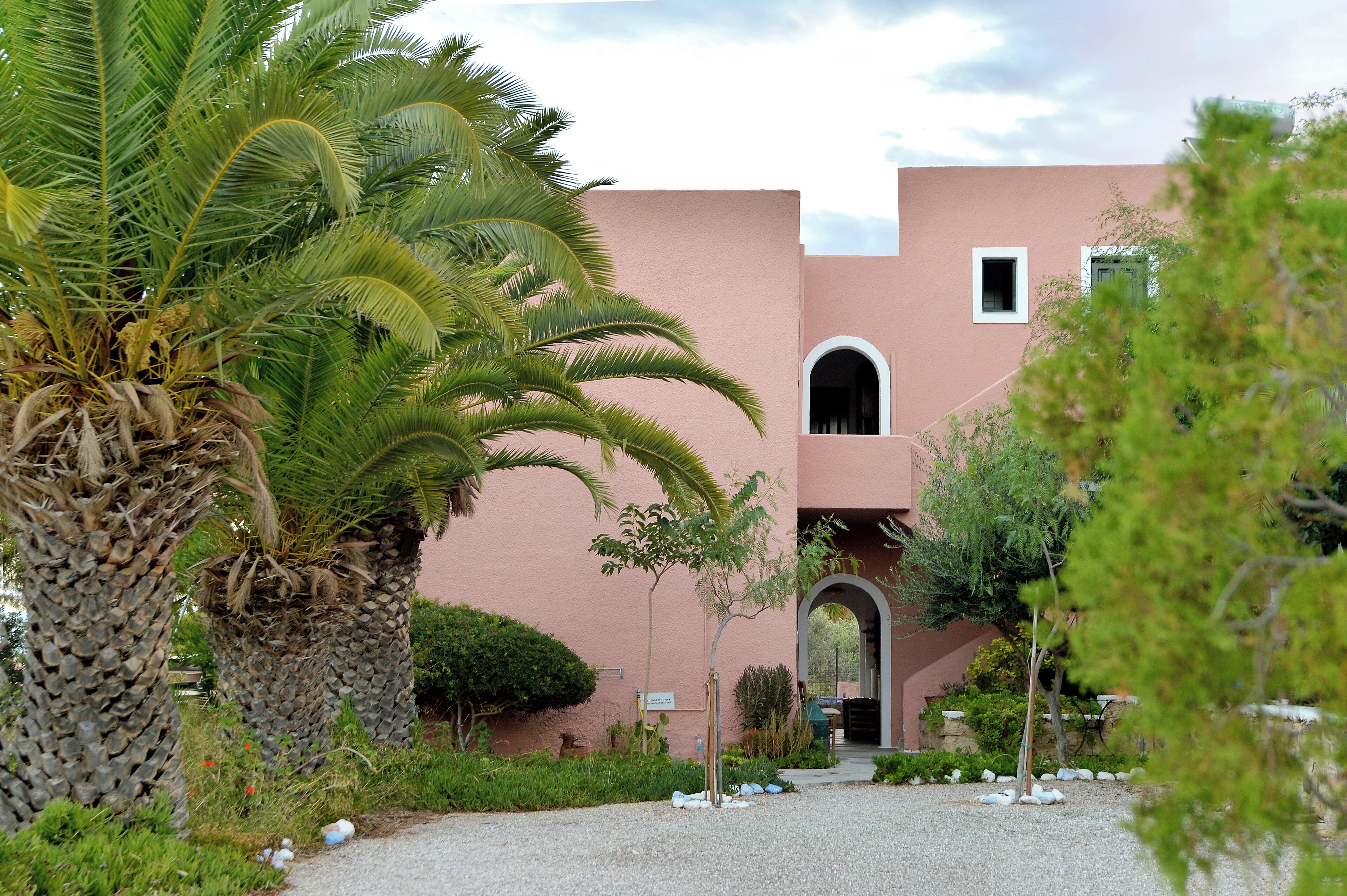 A building with a pink facade, palm trees, and a gravel pathway.