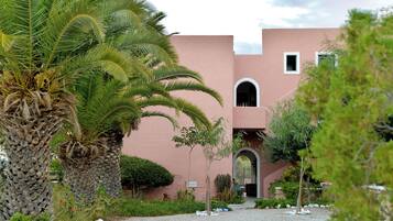 A building with a pink facade, palm trees, and a gravel pathway.