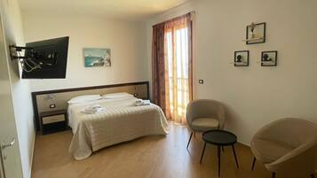 Ein Hotelzimmer mit einem Bett, einem Sessel, einem kleinen Tisch, einem Fernseher und Kunstwerken an den Wänden.