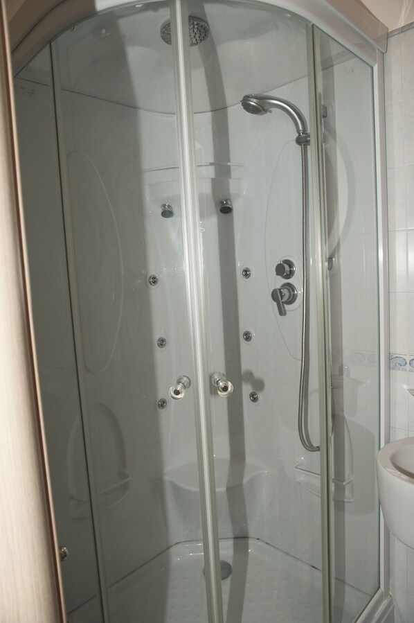 A glass-enclosed shower stall with a handheld showerhead and a wall-mounted faucet. - Albergo Perseo (Portopalo di Capo Passero)