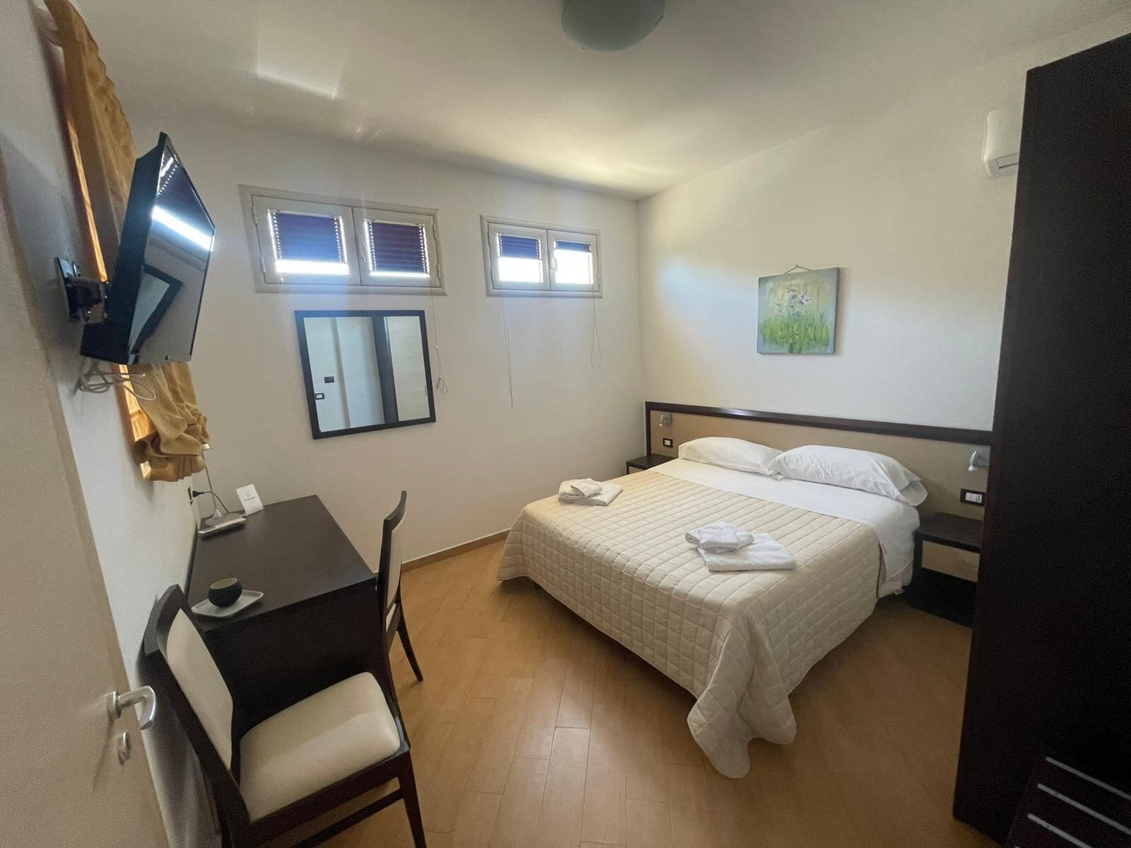 Hotelkamer met een bed, een bureau met stoel, een televisie en een schilderij aan de muur.