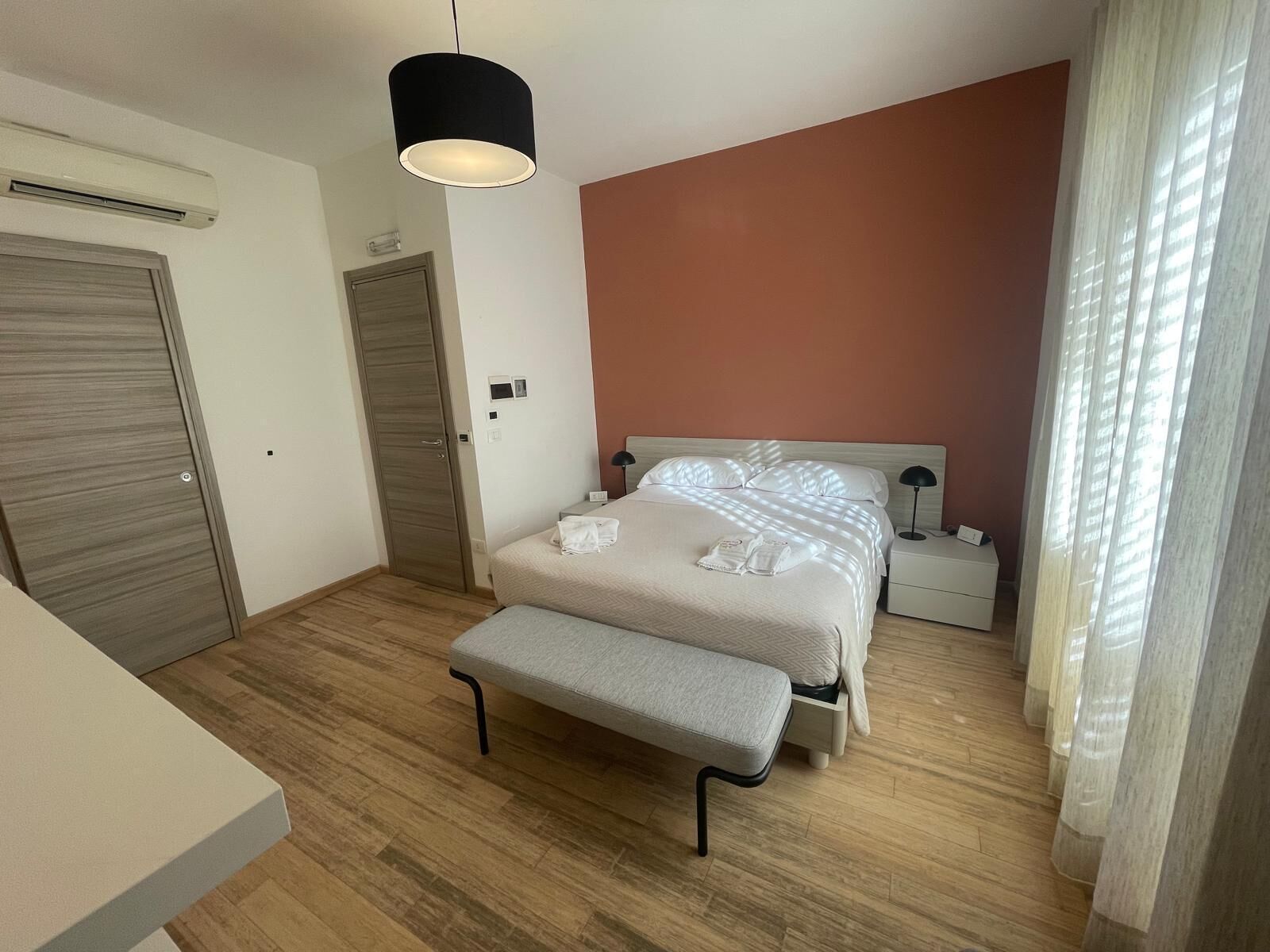 Ein Schlafzimmer mit Bett, Nachttischen, einer Bank, einer Klimaanlage und einer Tür.