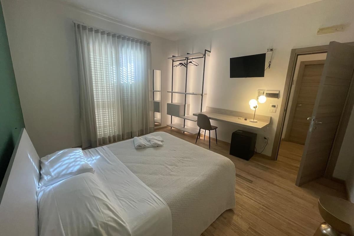 A hotel room with a bed, a desk, a chair, a TV, and a wardrobe.