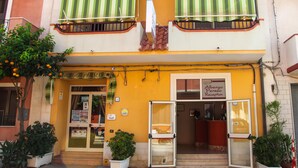A yellow building with a reception area, a balcony with green striped awnings, and potted plants.