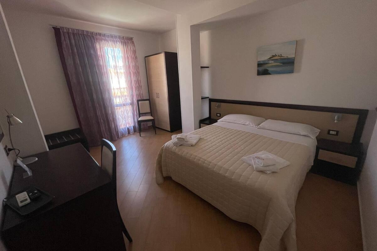Una habitación de hotel con cama, escritorio, silla, armario y un cuadro en la pared.