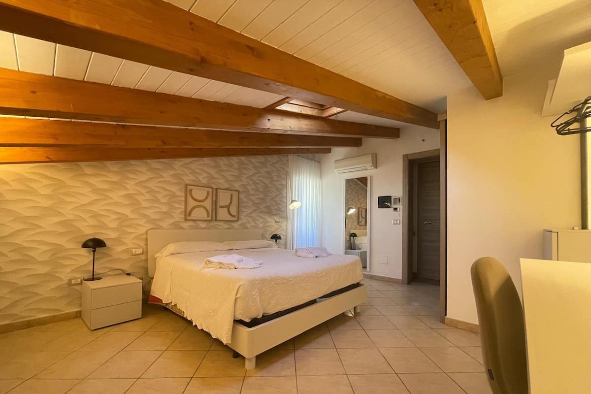 A bedroom with a bed, bedside table, lamp, and a door leading to another room.