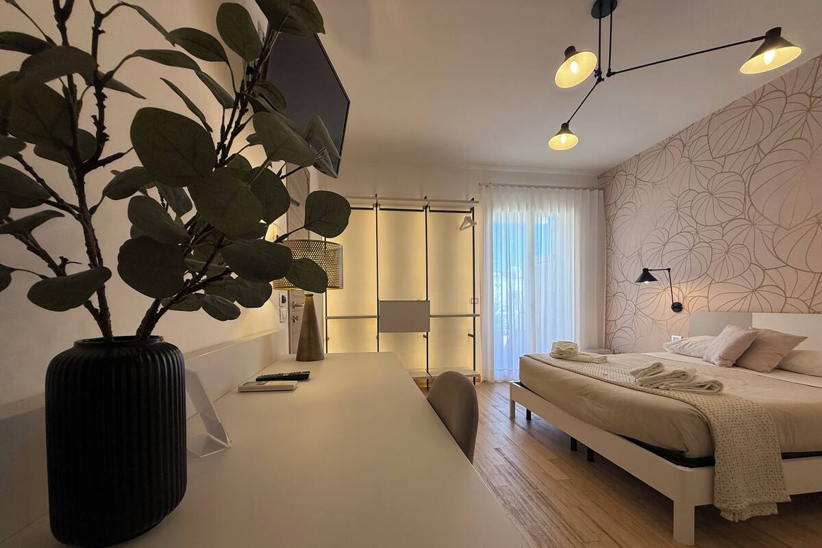 Habitación de hotel moderna con cama, mesita de noche y una planta grande en maceta.