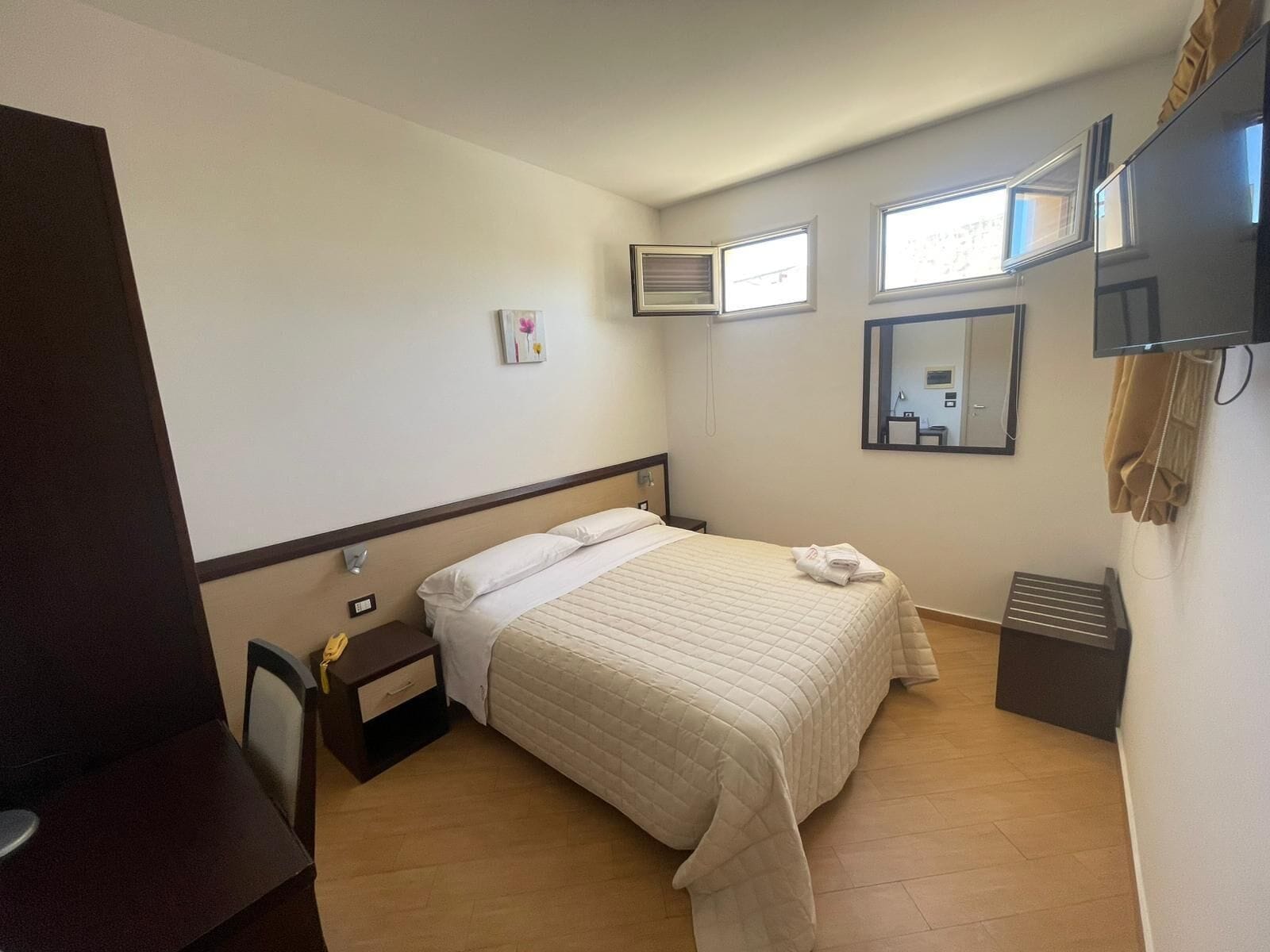 Ein Hotelzimmer mit Bett, Nachttisch, Spiegel, Fernseher und Fenster.
