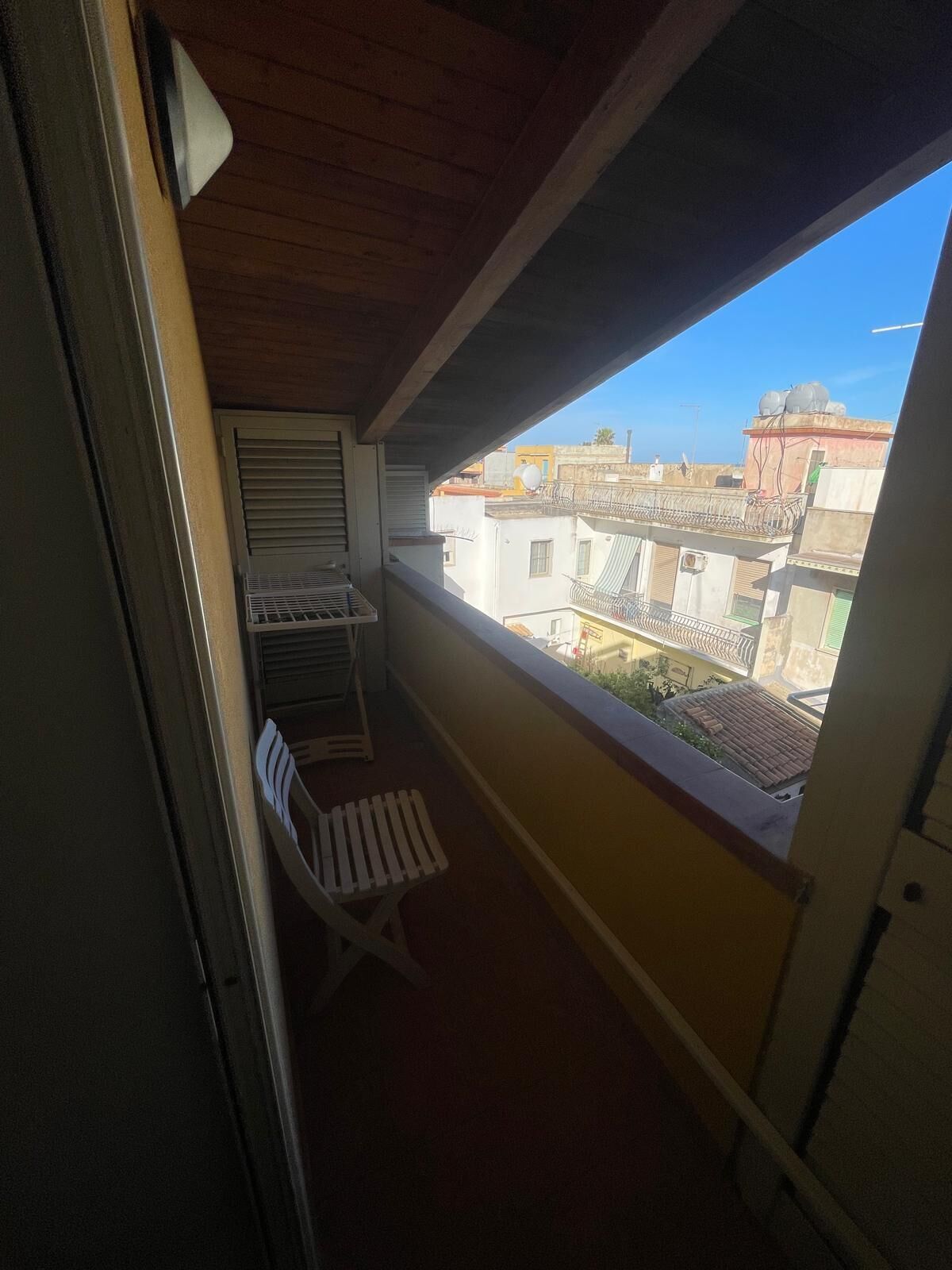 Un balcón con una silla blanca, una mesita y una ventana con vistas a la ciudad.