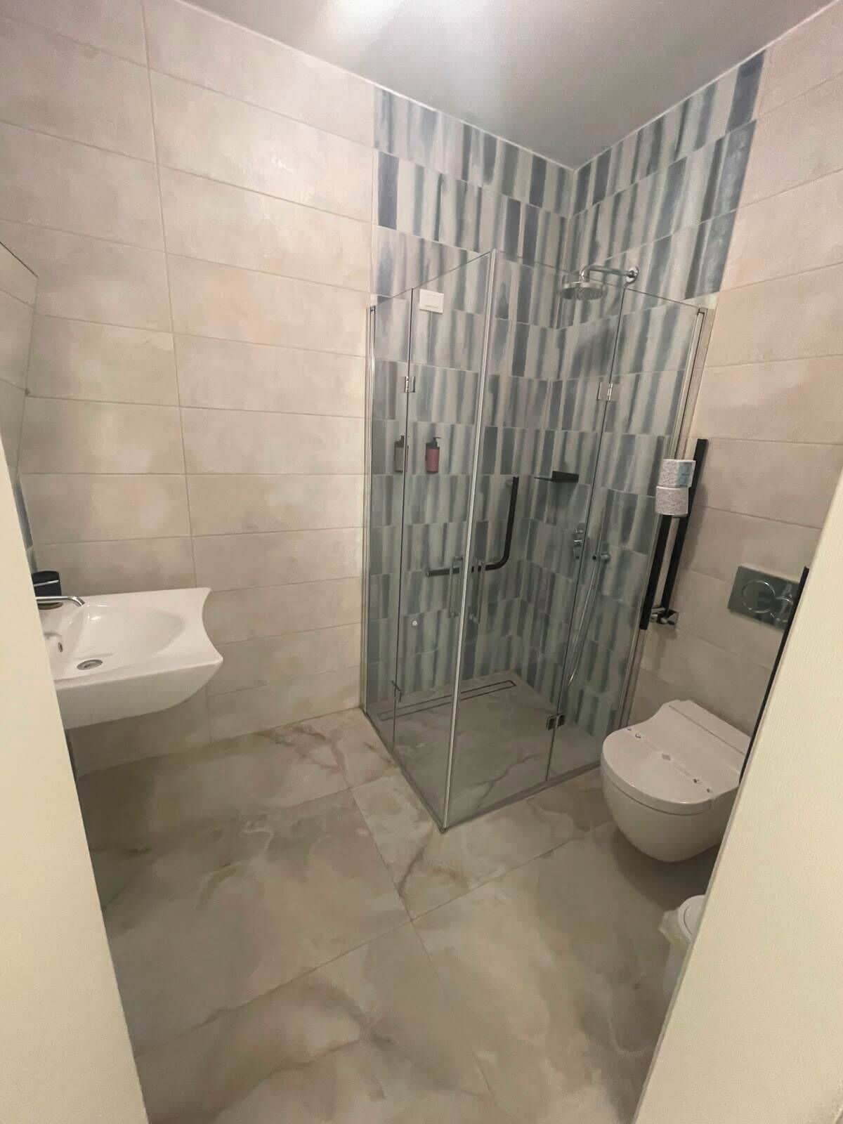 Un bagno con doccia vetrata, lavandino bianco e water.