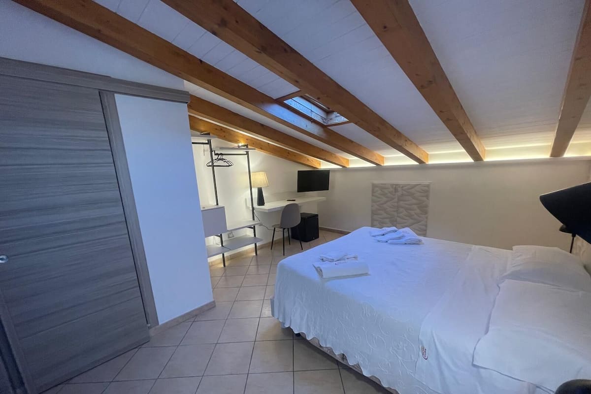 A modern bedroom with a large bed, a desk, and a TV.