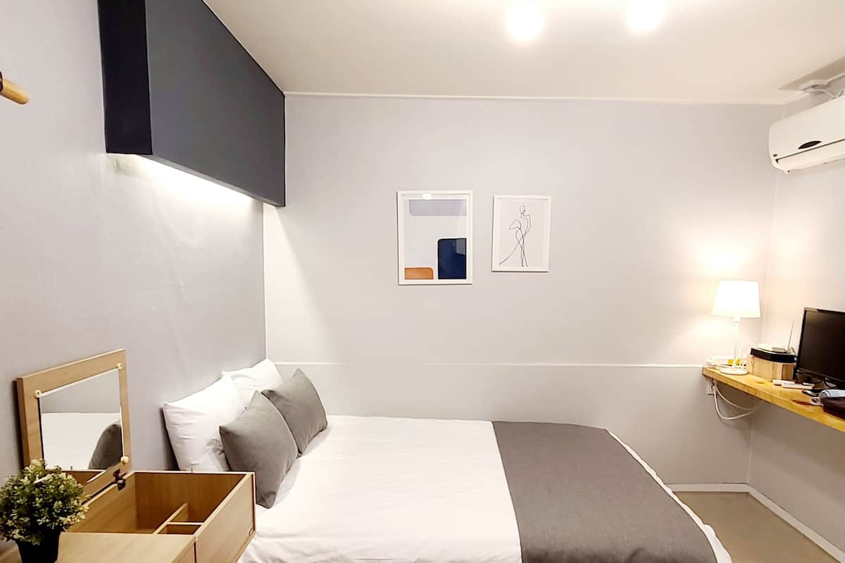 A hotel room with a bed, bedside table, TV, and an air conditioning unit.