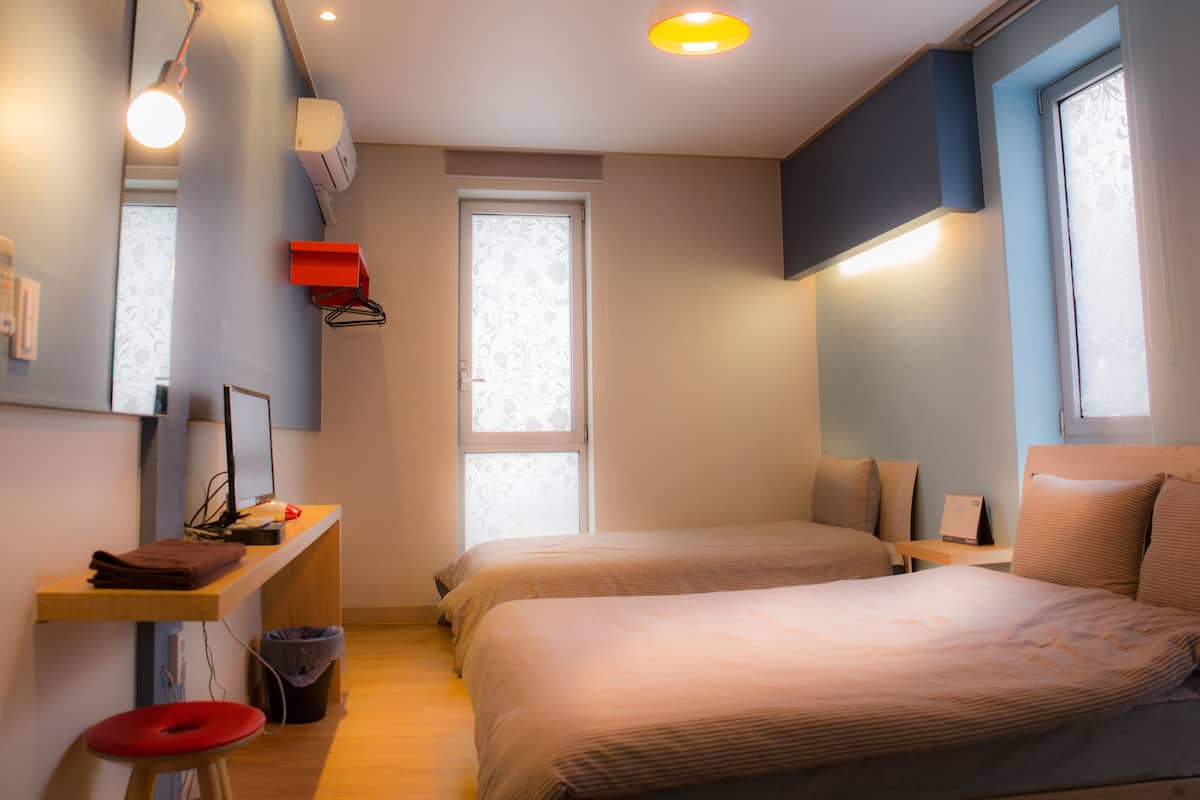 A bedroom with two beds, a desk with a computer, a chair, and a window.