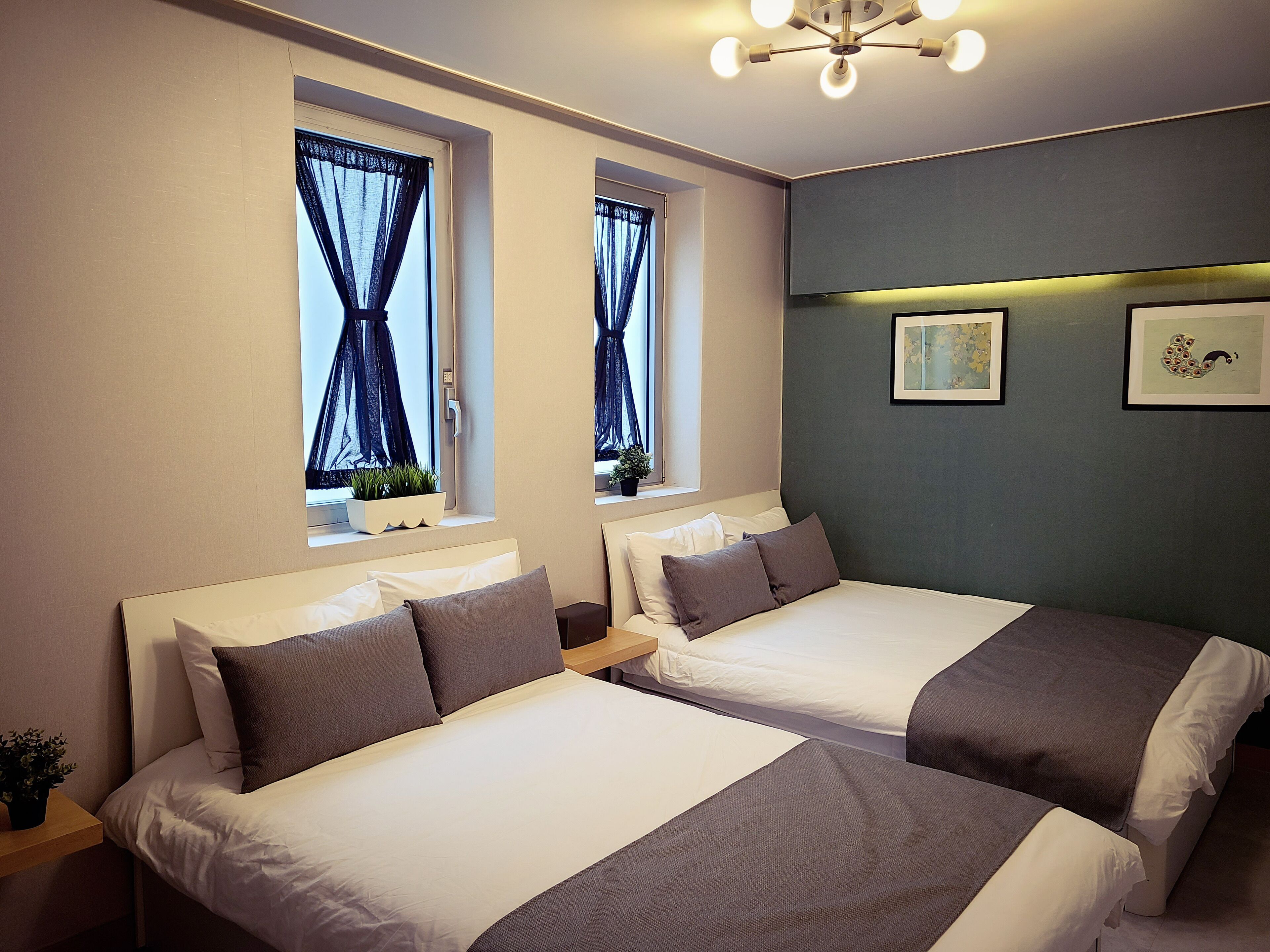 A hotel room with two beds, a ceiling light, and artwork on the wall.