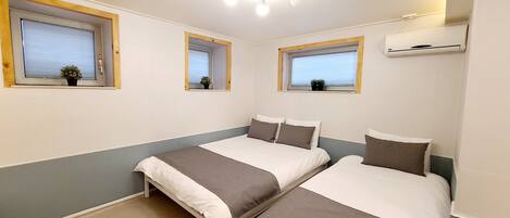 A room with two beds, a ceiling light fixture, and three windows with wooden frames.