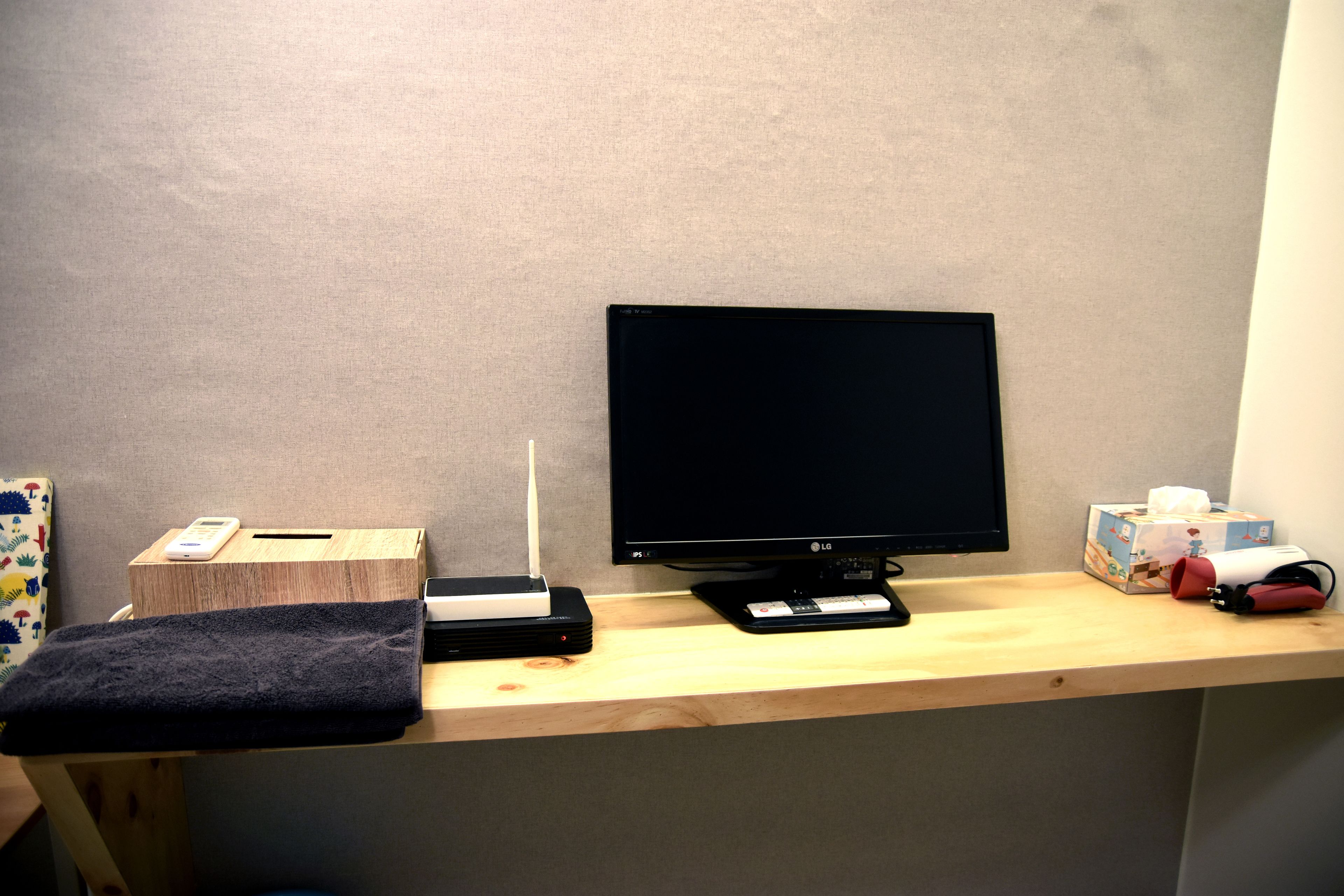 A wooden desk with a computer monitor, a smartphone, a box, and a tissue box.