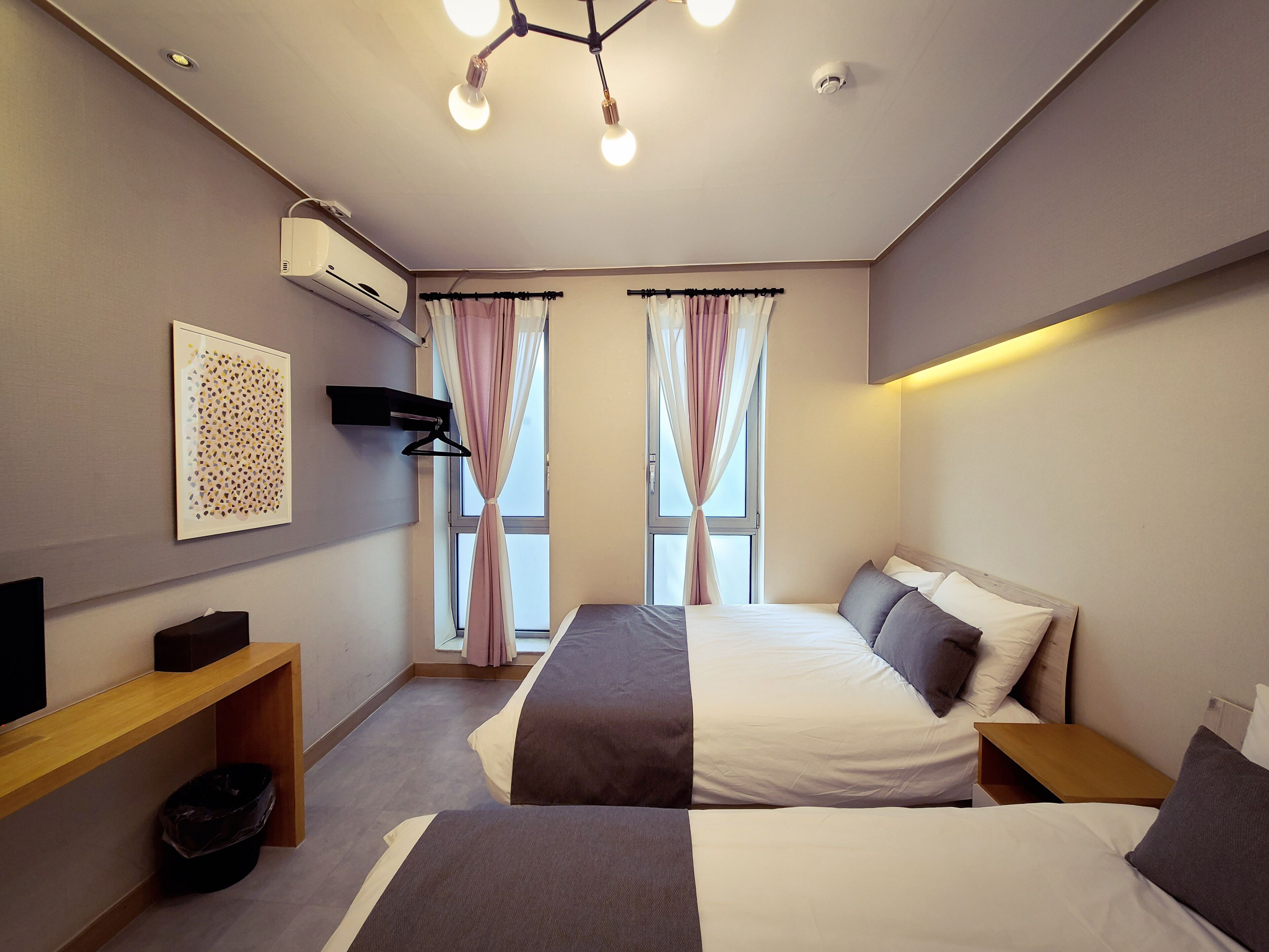 A modern hotel room with a large bed, bedside tables, a TV, and a ceiling light fixture.