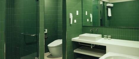 Un baño con azulejos verdes, cabina de ducha de vidrio, inodoro, lavabo y bañera.