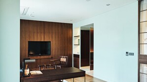Una sala de estar moderna con un televisor de pantalla plana montado en una pared de madera, un comedor con una mesa y sillas de madera oscura, y una cocina visible con gabinetes de madera.