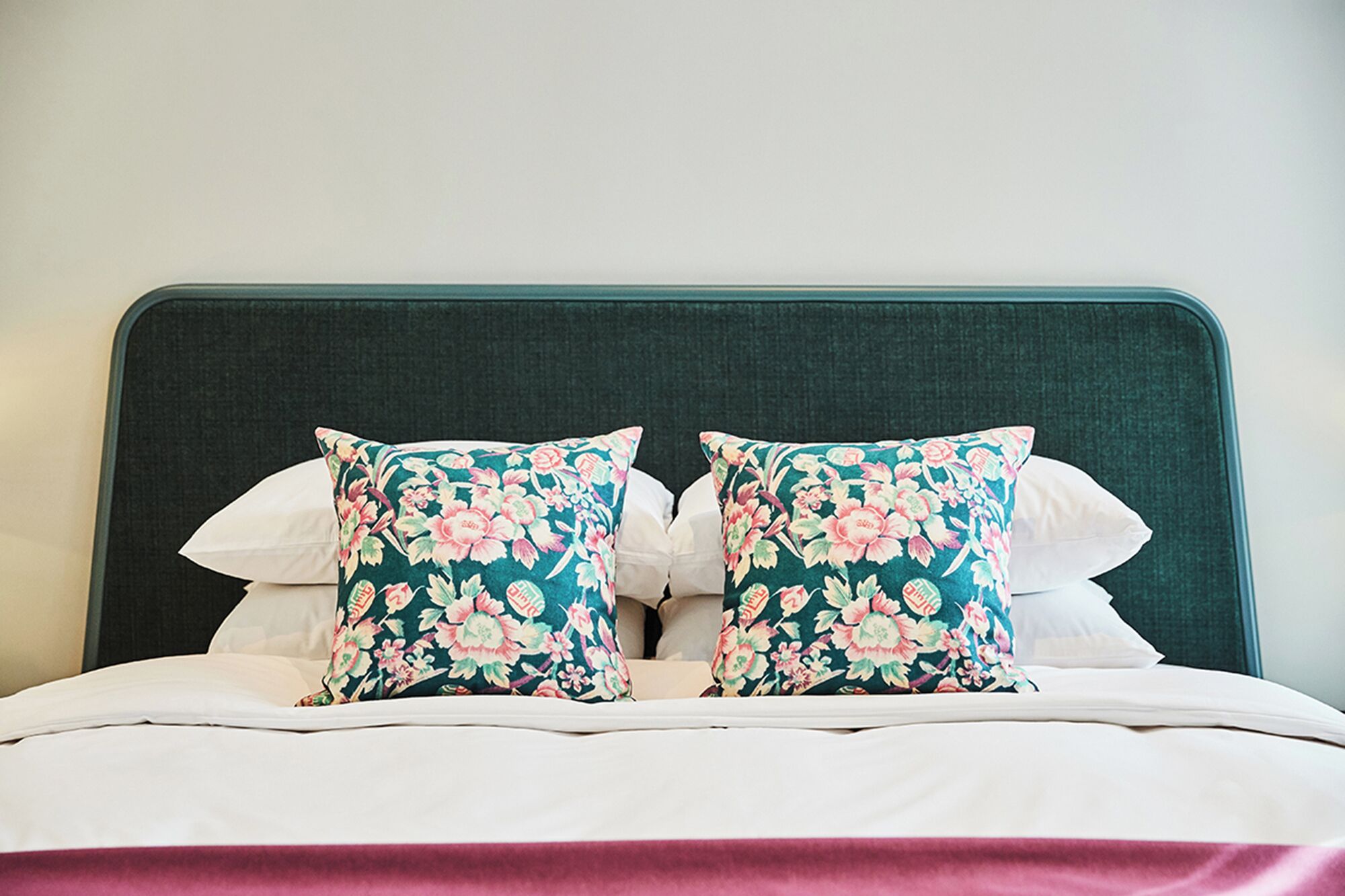 A bed with a dark headboard, two floral pillows, and a white bedspread.