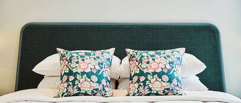 A bed with a dark headboard, two floral pillows, and a white bedspread.